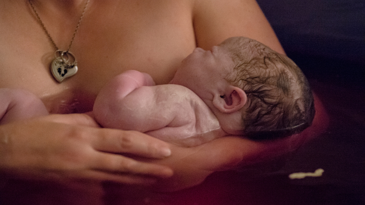 Mother cradles newborn with vernix in water